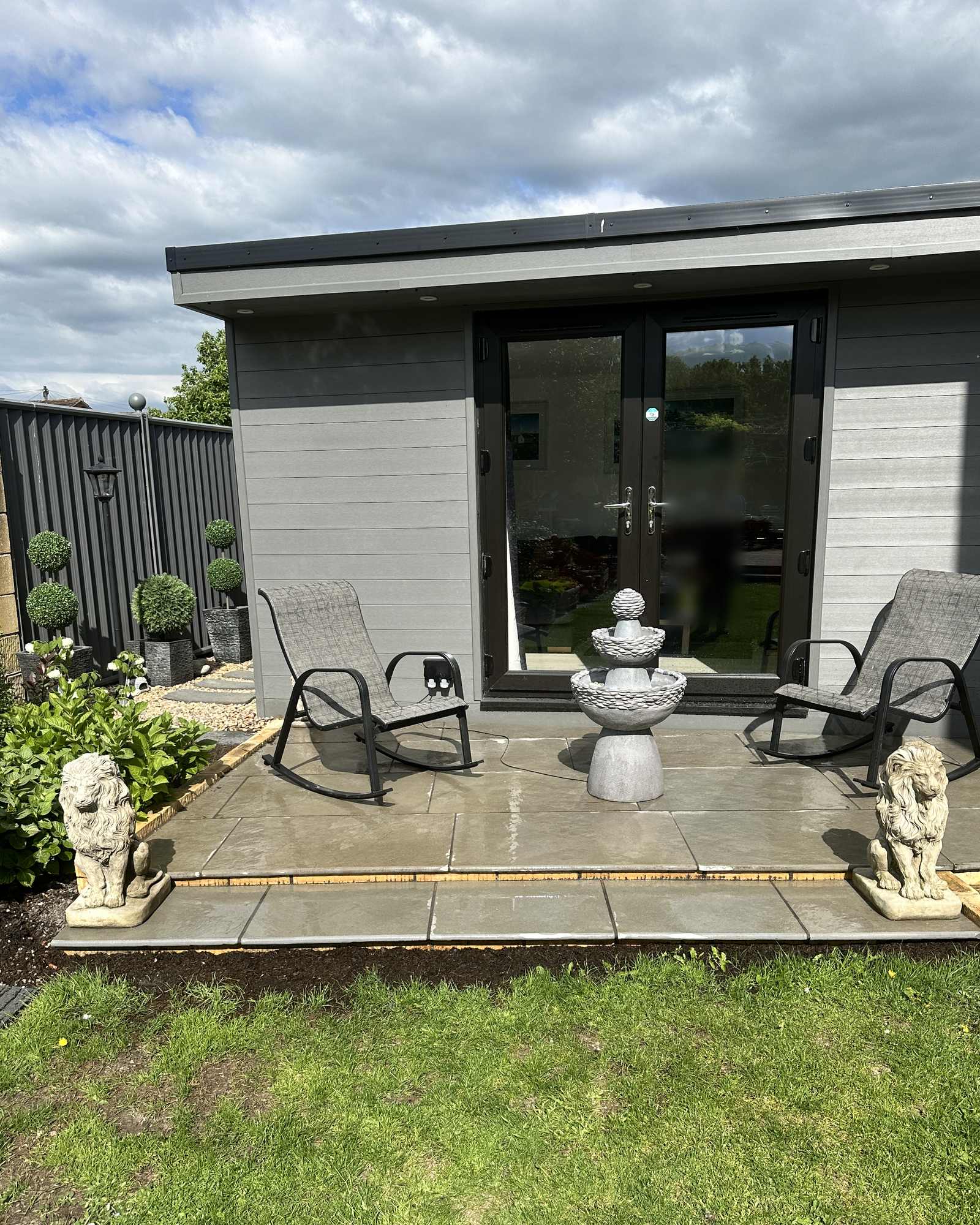 Finished grey patio with outdoor seating beside a garden room.
